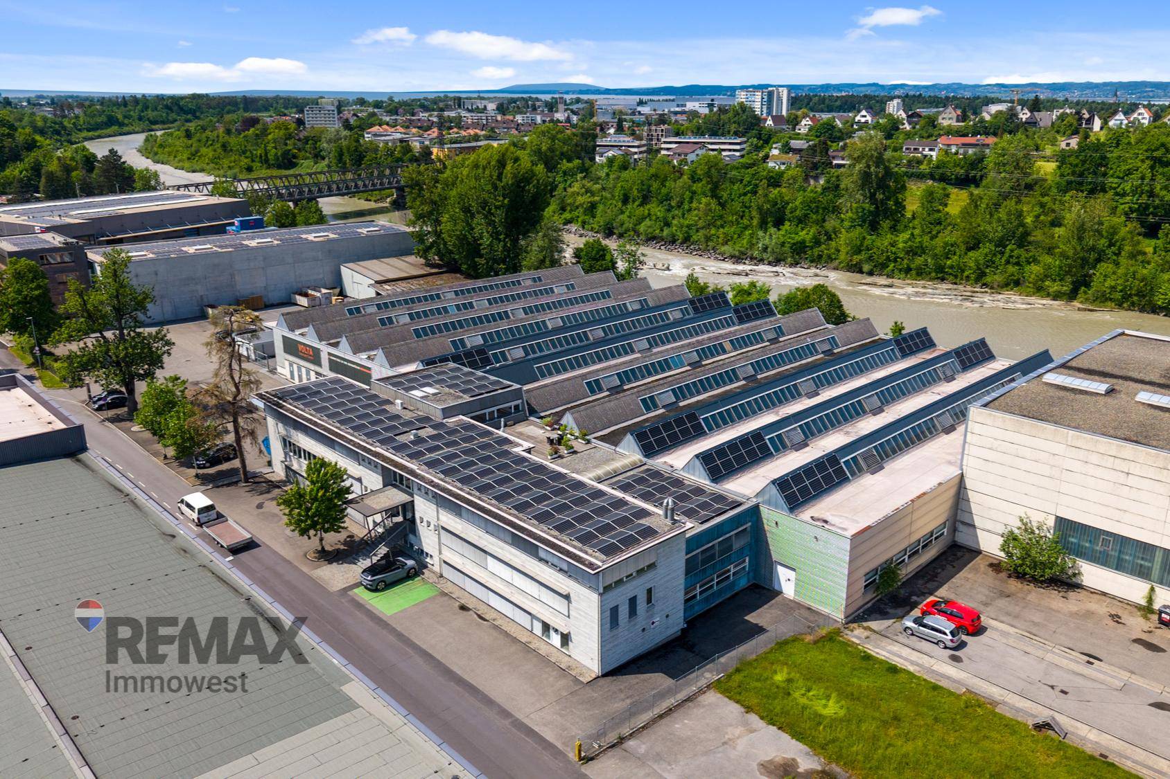 Weitläufige Luftaufnahme des Industrieareals mit Solaranlagen auf den Dächern, Fluss und umliegender Stadt.
