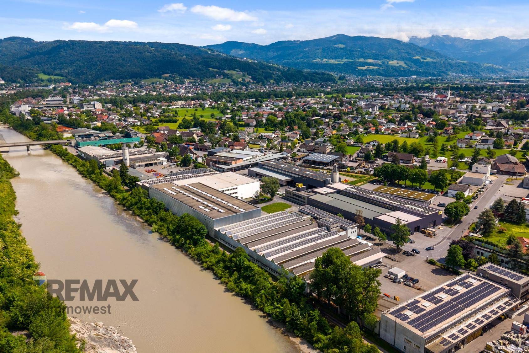 Panoramische Luftaufnahme des Industriegebiets am Flussufer, umgeben von einer Stadt und grünen Bergen.