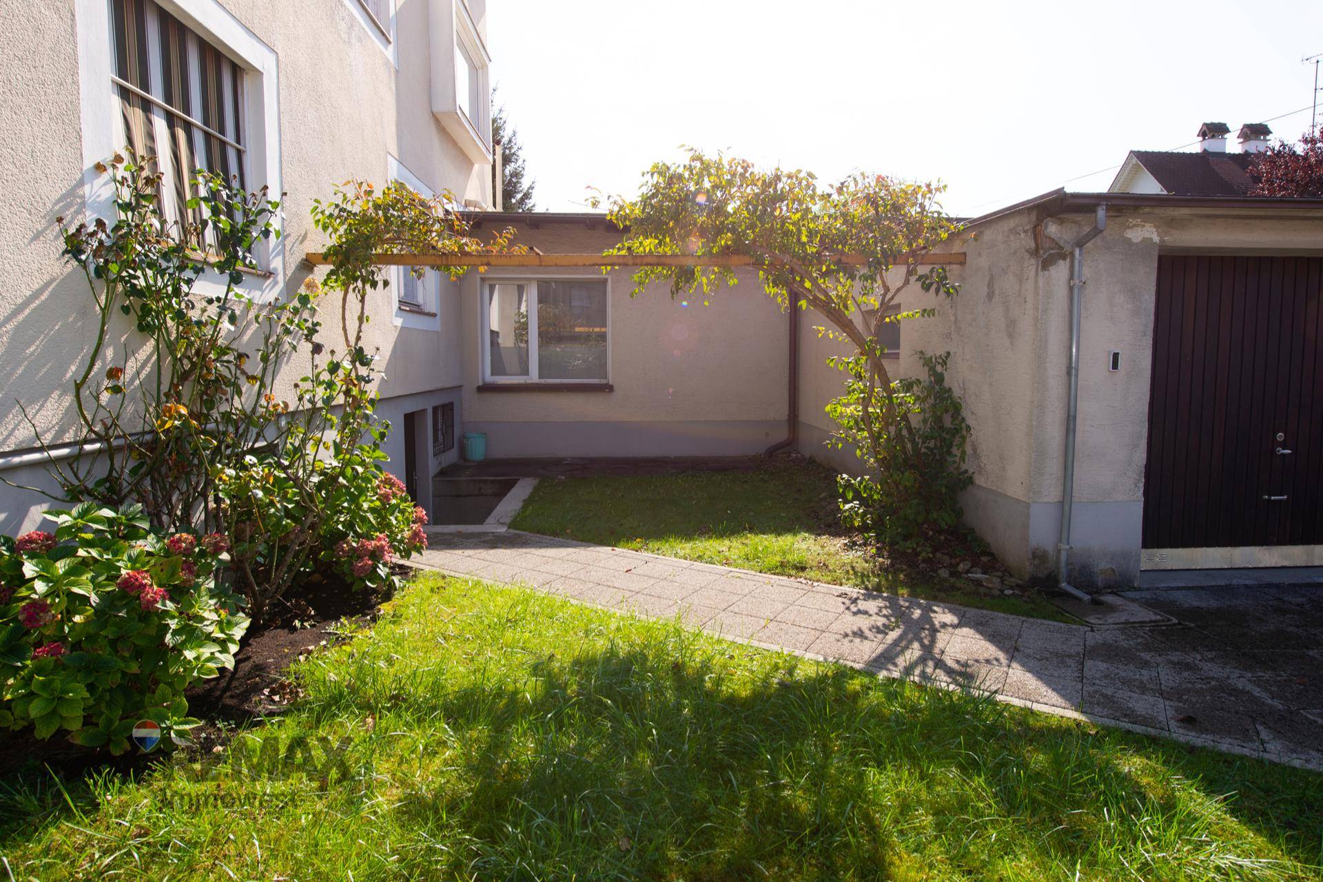 Kleiner Gartenbereich neben dem Haus mit Zugang zum Keller und einer Garage.