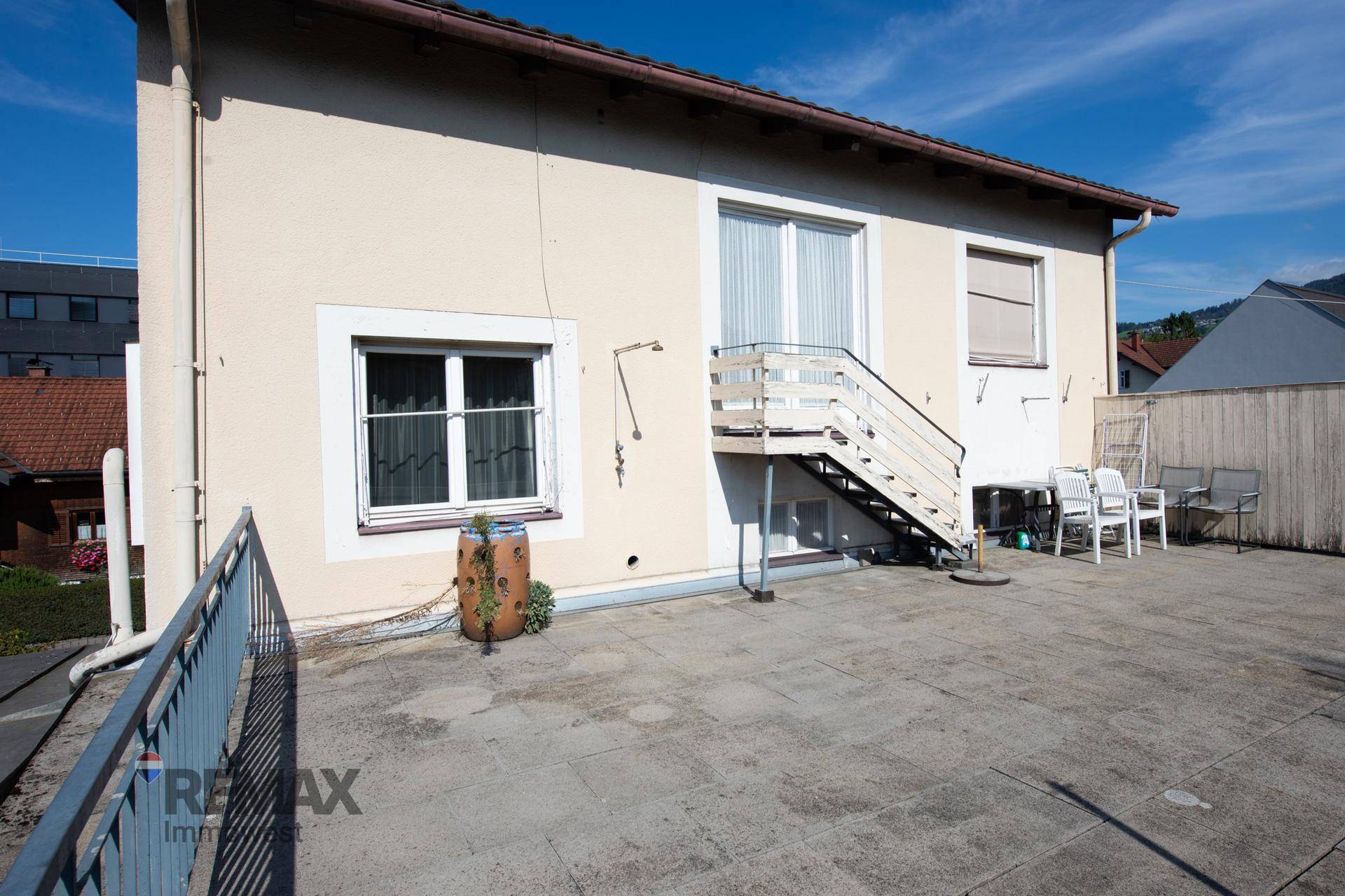 Geräumige gepflasterte Terrasse hinter dem Haus mit Treppe und Sitzgelegenheiten im Freien.