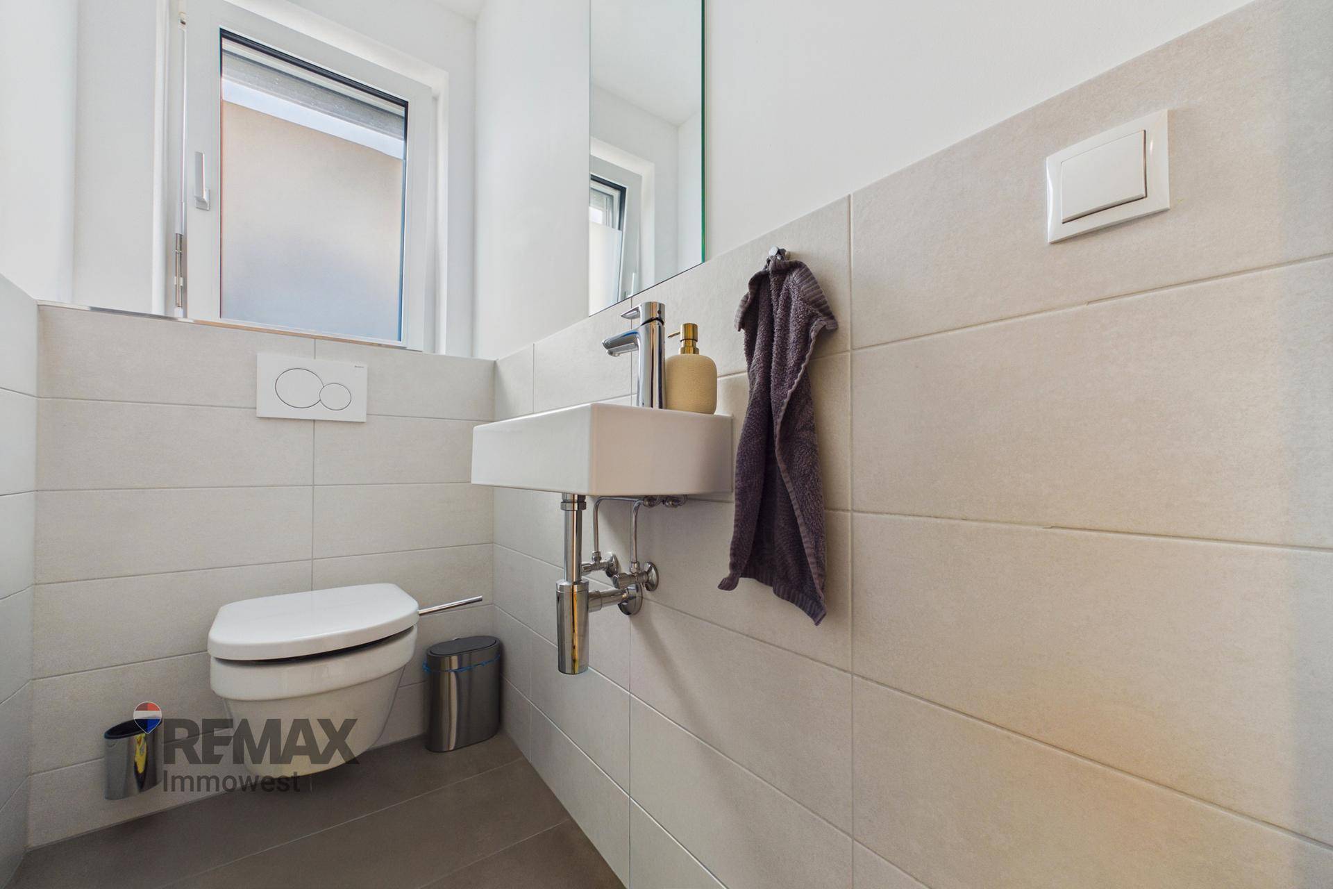 Modernes Gäste-WC mit wandhängender Toilette, kleinem Waschbecken und Fenster.