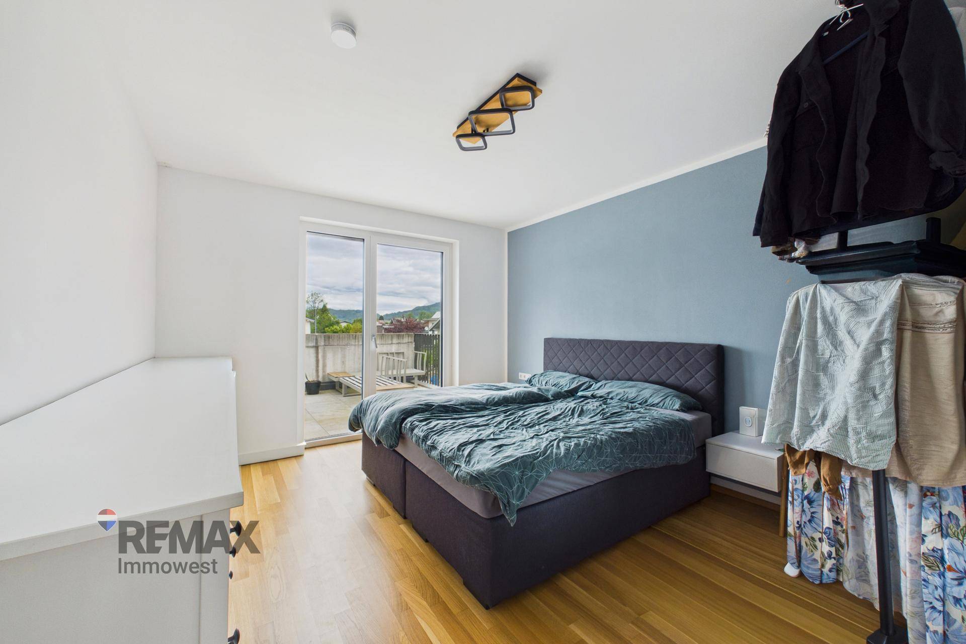 Schlafzimmer mit Doppelbett, blauer Akzentwand und Zugang zum Balkon.