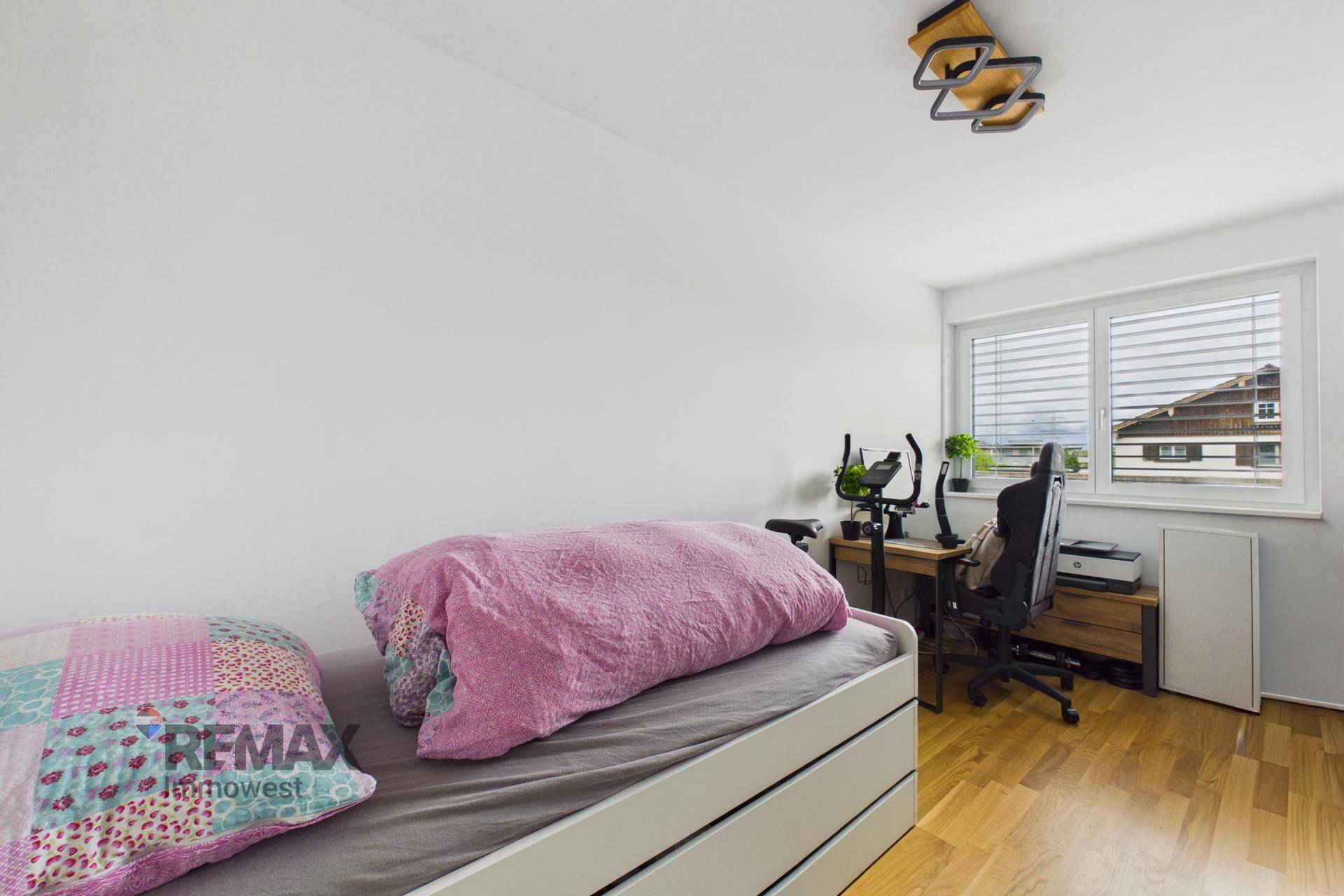 Helles Schlafzimmer mit Einzelbett, Schreibtisch und Holzparkettboden.