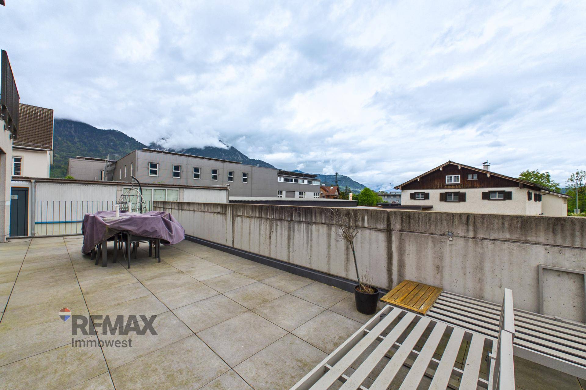 Große Dachterrasse mit Sitzgelegenheiten und Liegestühlen unter bewölktem Himmel.