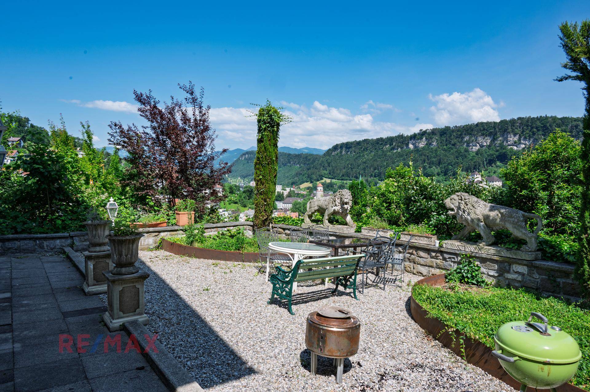 Mediterraner Gartenbereich mit Kiesfläche, Sitzgelegenheiten und dekorativen Löwenstatuen mit Bergblick.