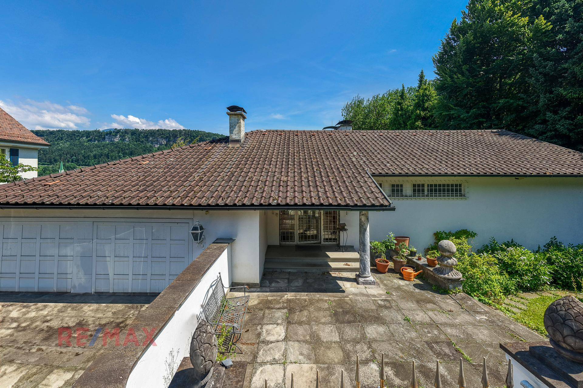Eingangsbereich und Garage der Villa mit gepflastertem Vorplatz und mediterranen Pflanzen.