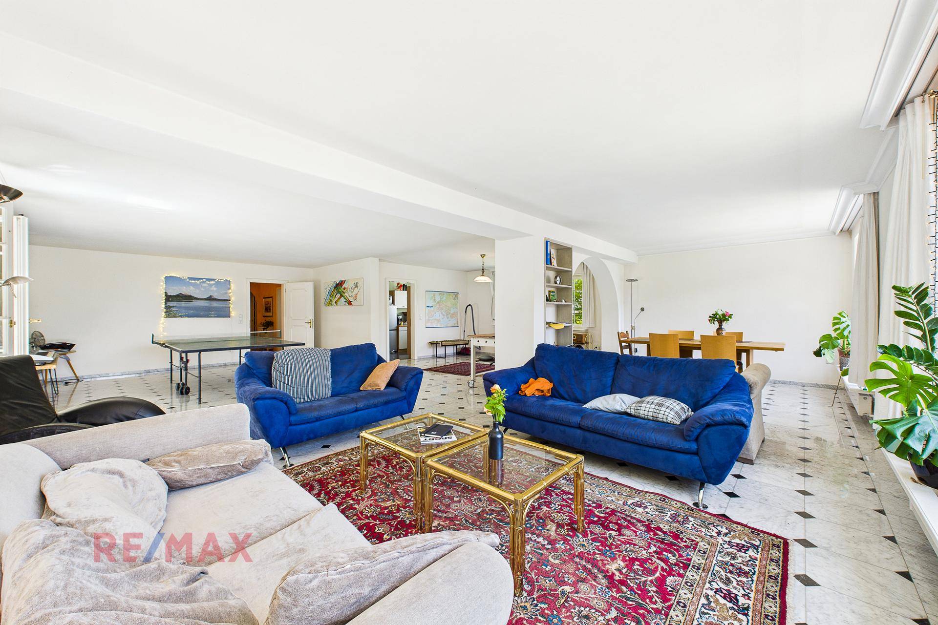 Großzügiger Wohn- und Essbereich mit Marmorboden, blauen Sofas und einem Esstisch im Hintergrund.