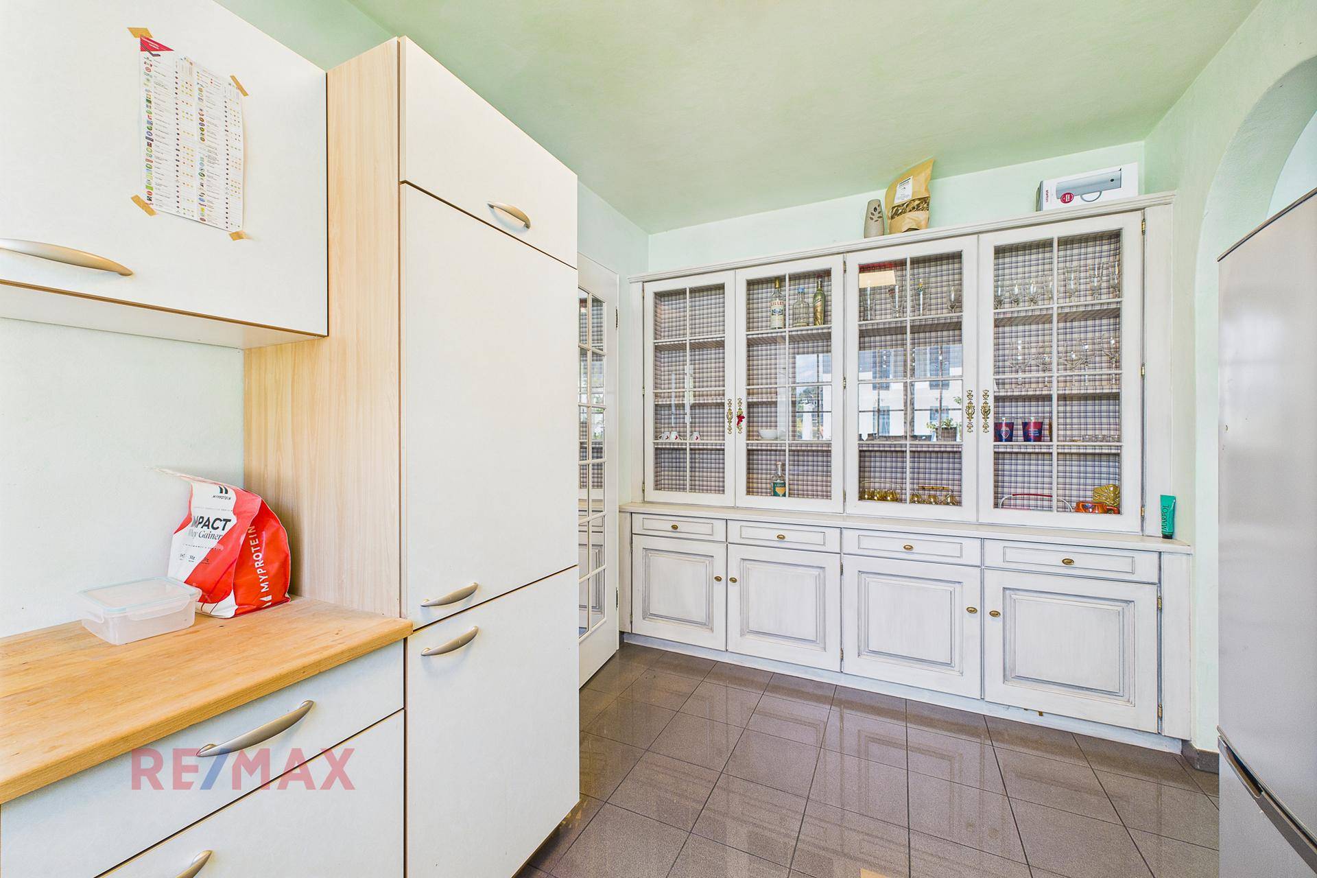 Küchenzeile mit weißen Schränken, Holztheke und großem Vitrinenschrank.