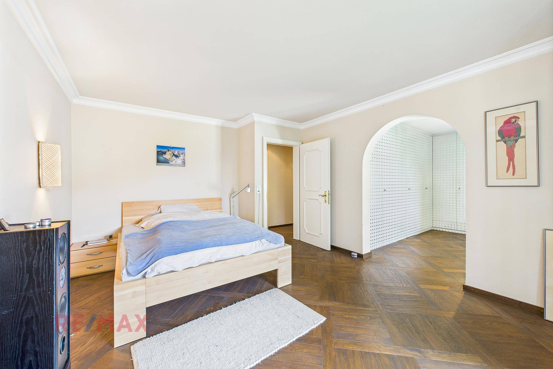 Helles Schlafzimmer mit Parkettboden, Doppelbett und Zugang zu einem Ankleidebereich.