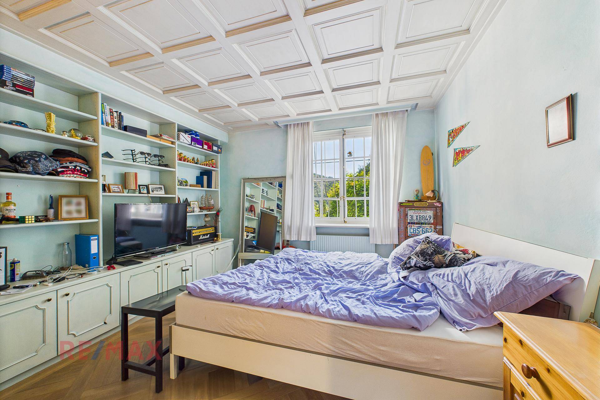 Schlafzimmer mit Kassettendecke, Einbauregalen und Fenster mit Blick ins Grüne.