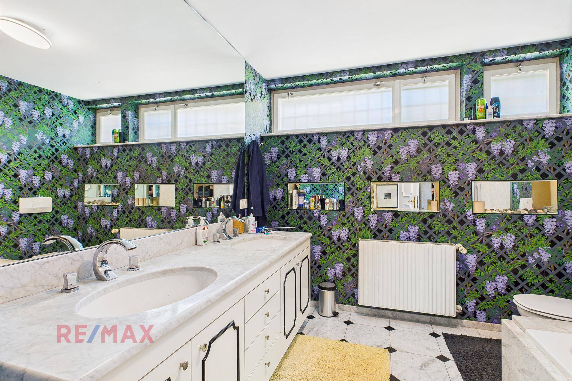 Geräumiges Badezimmer mit floraler Tapete, Doppelwaschbecken und Marmoroberflächen.