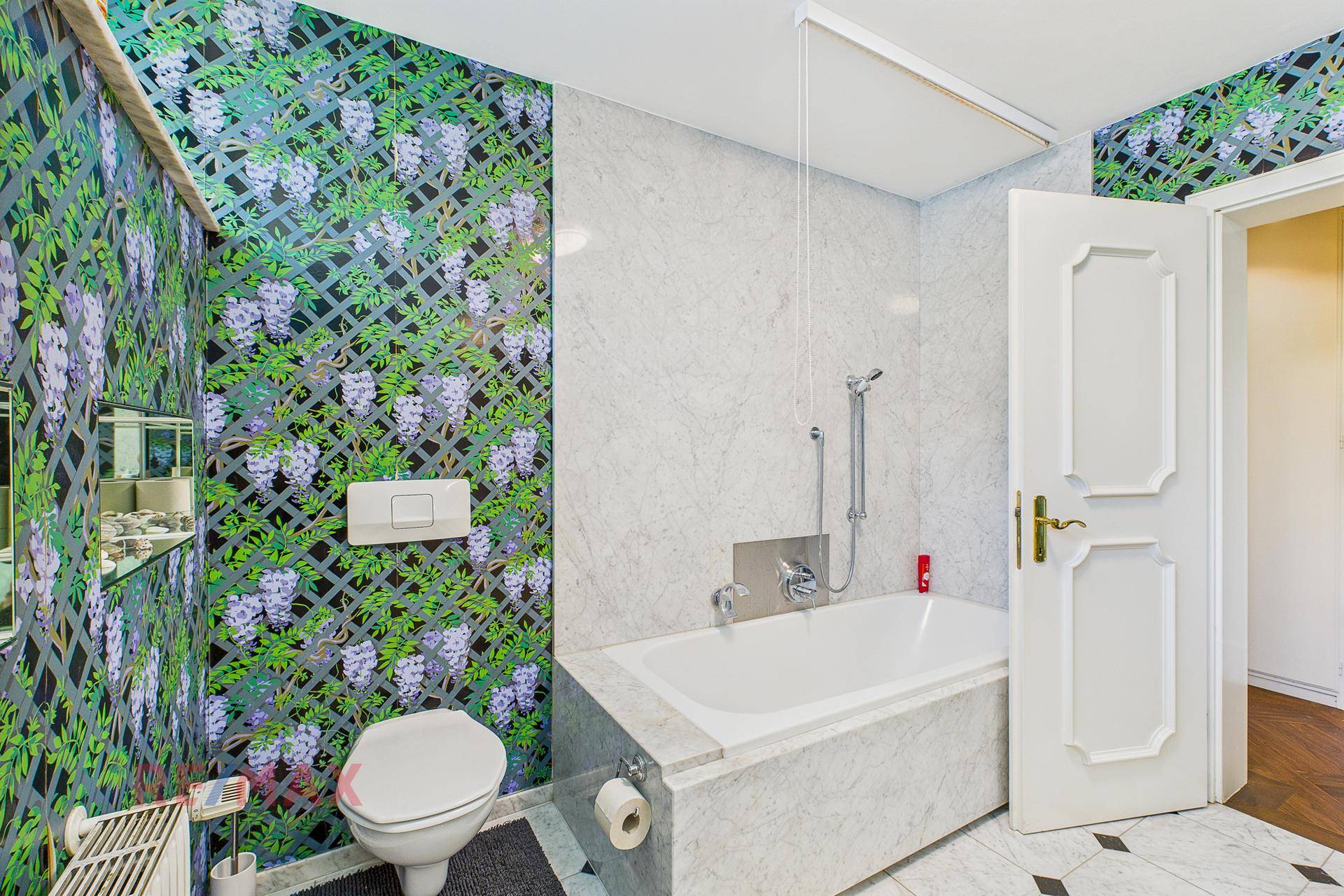 Badezimmer mit floraler Tapete, eingebauter Badewanne und Wand-WC.