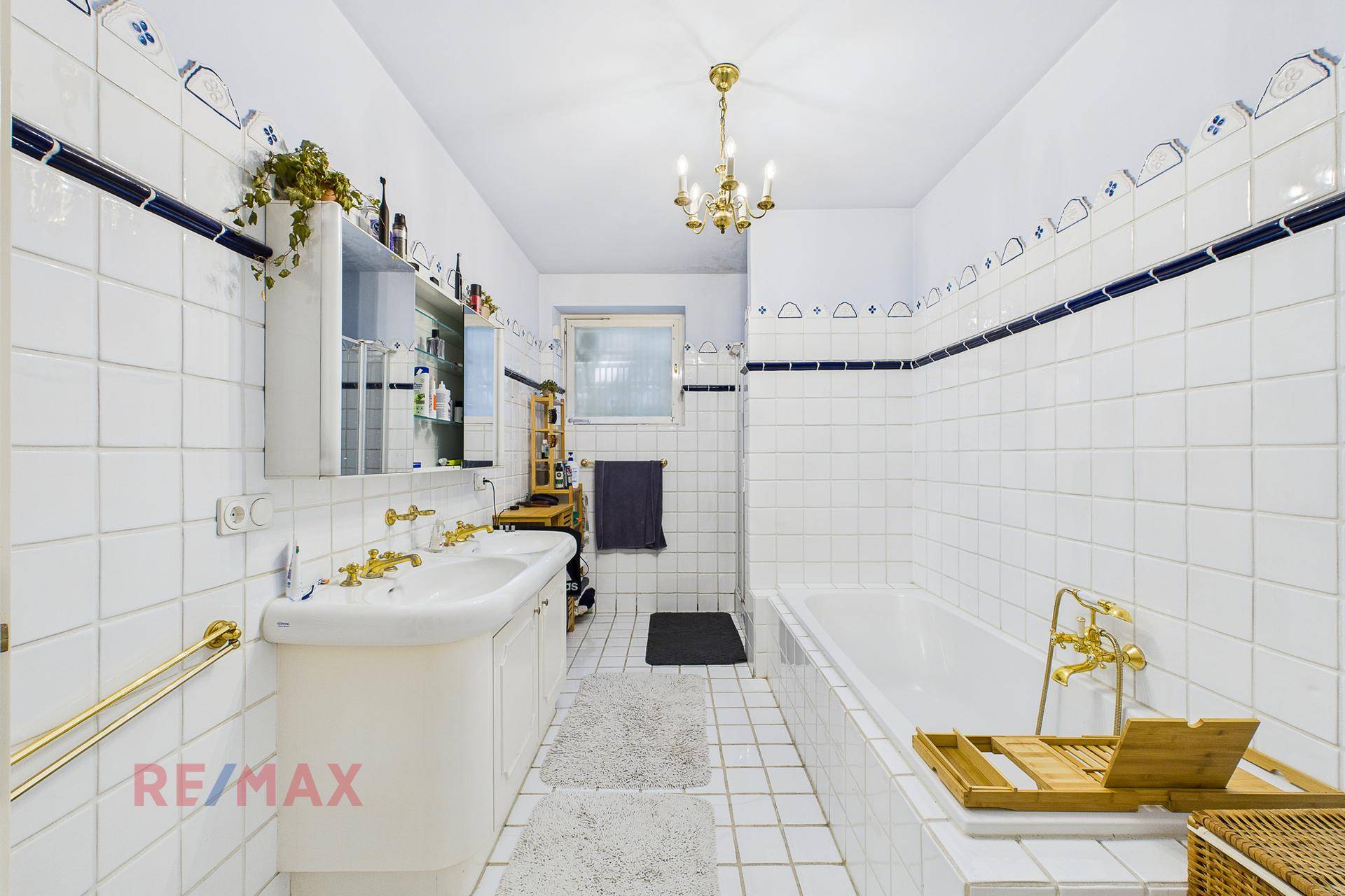 Helles Badezimmer mit weißen Fliesen, Badewanne, Doppelwaschbecken und goldenen Armaturen.
