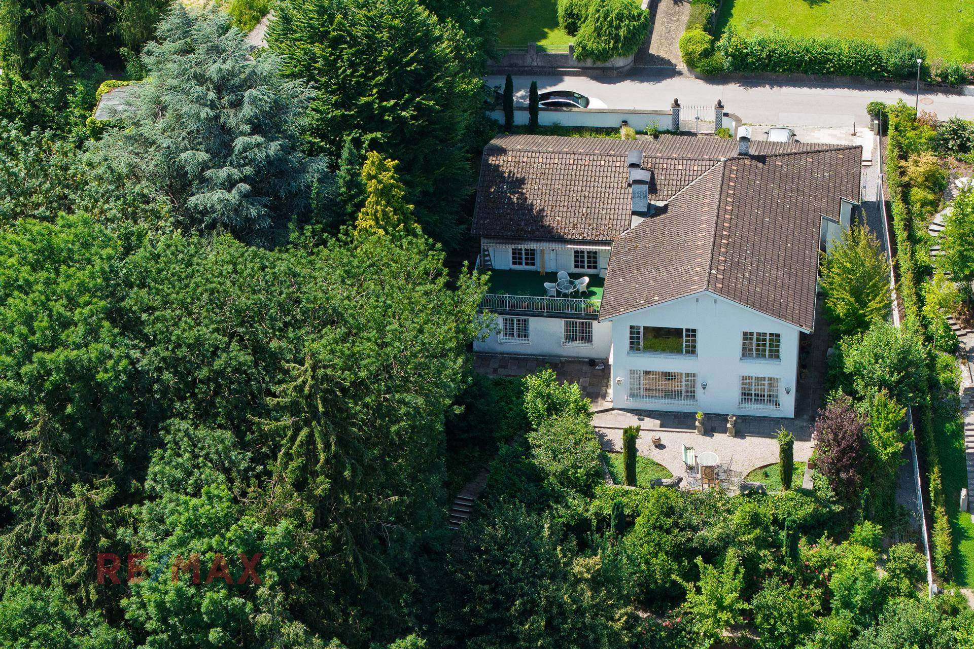 Luftaufnahme eines Hauses umgeben von üppigem Grün, mit einem möblierten Balkon und Terrasse.
