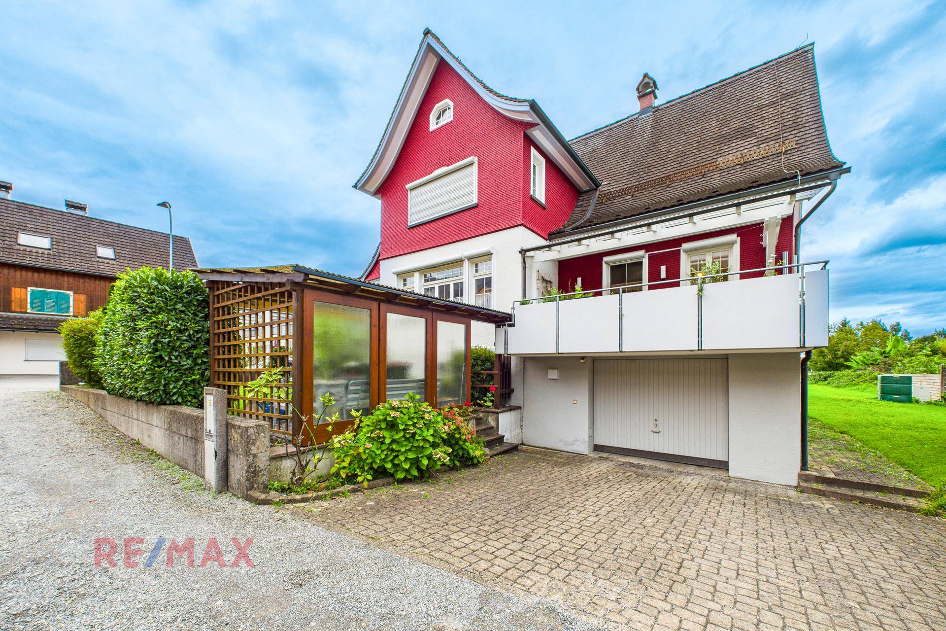 Rotes Haus mit Garage, Balkon und einem überdachten Anbau im Außenbereich.
