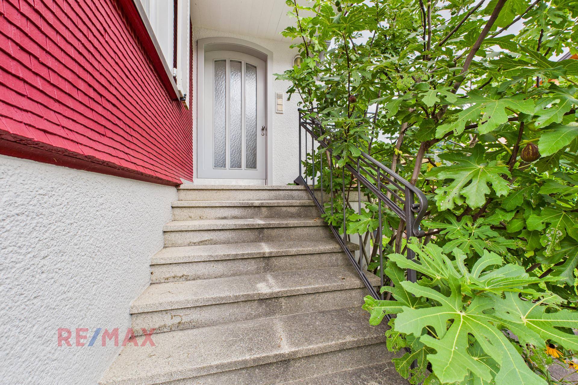 Steintreppe führt zum Hauseingang mit weißer Tür und schmiedeeisernem Geländer.