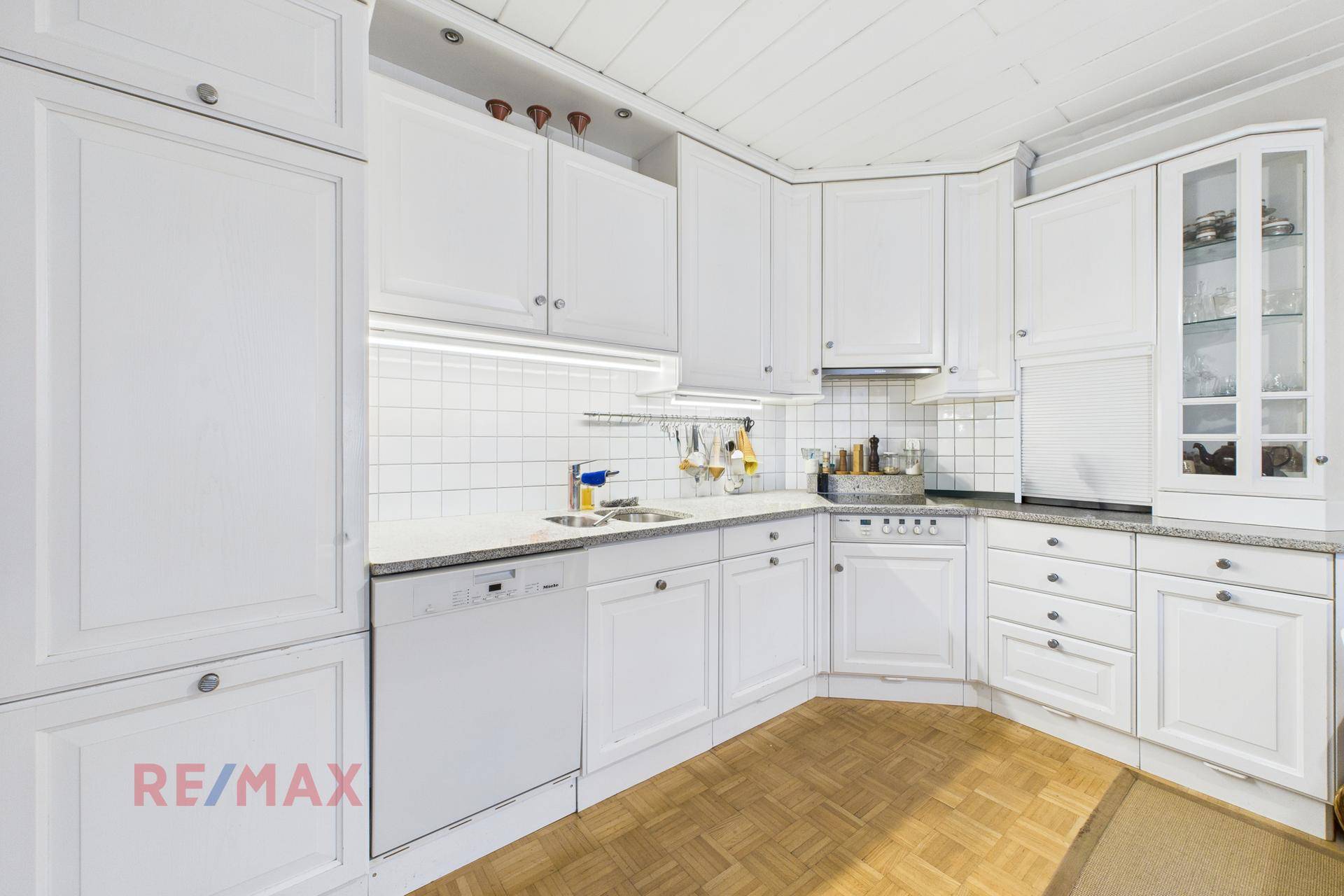 Weiße Einbauküche mit Holzdecke, Fliesenrückwand und integrierten Geräten.