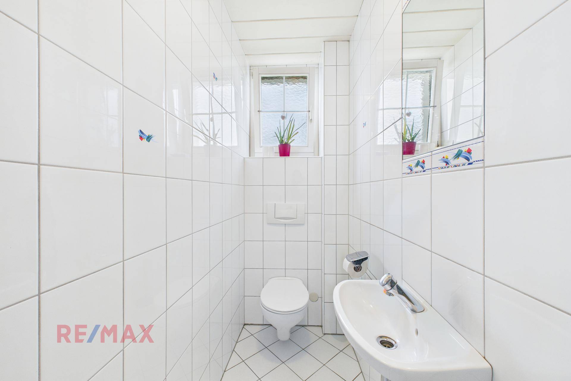 Kleines Gäste-WC mit weißen Fliesen, wandhängendem WC und kleinem Waschbecken.