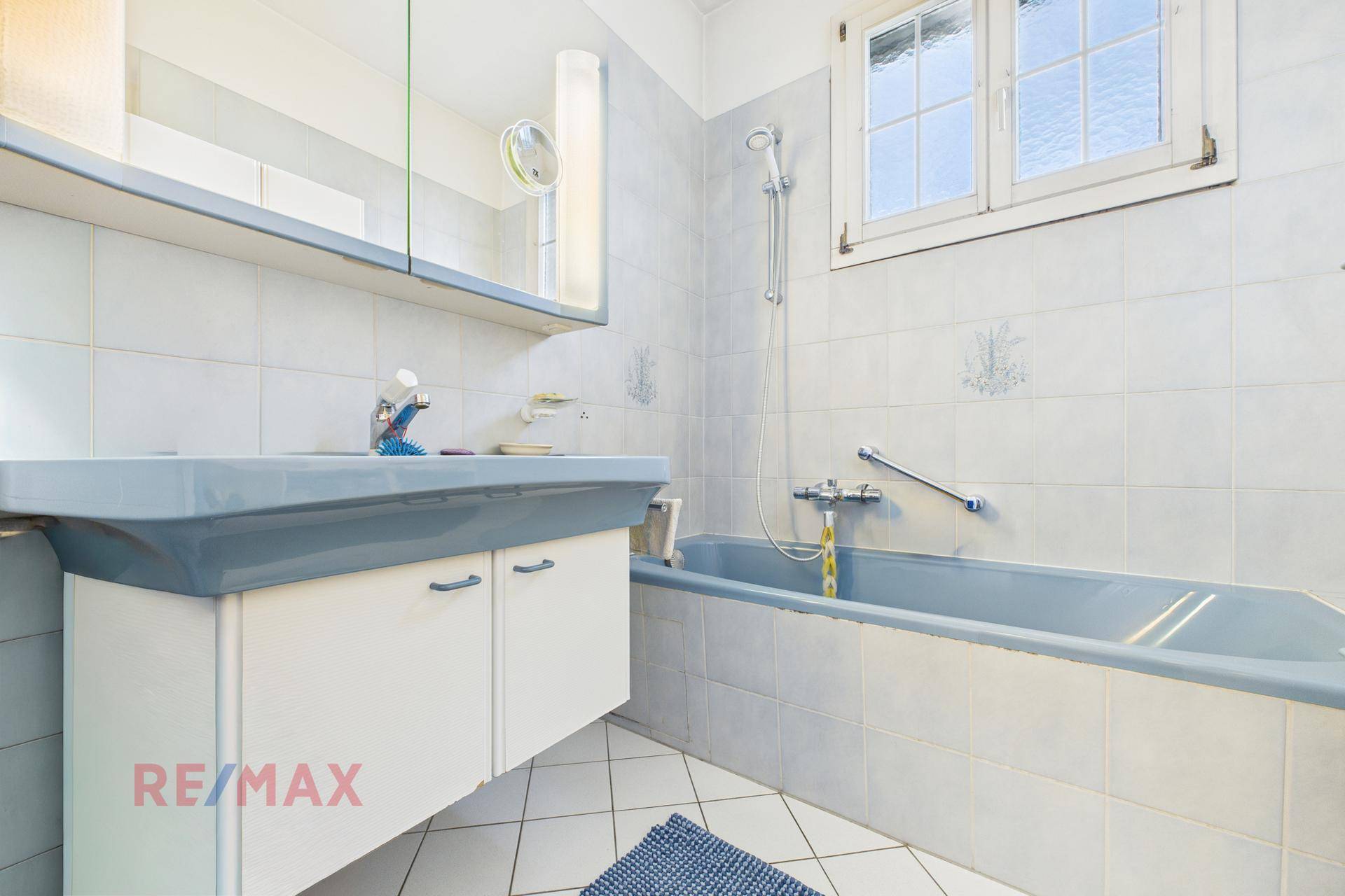 Badezimmer mit blauer Badewanne, Waschbecken und Spiegelschrank.