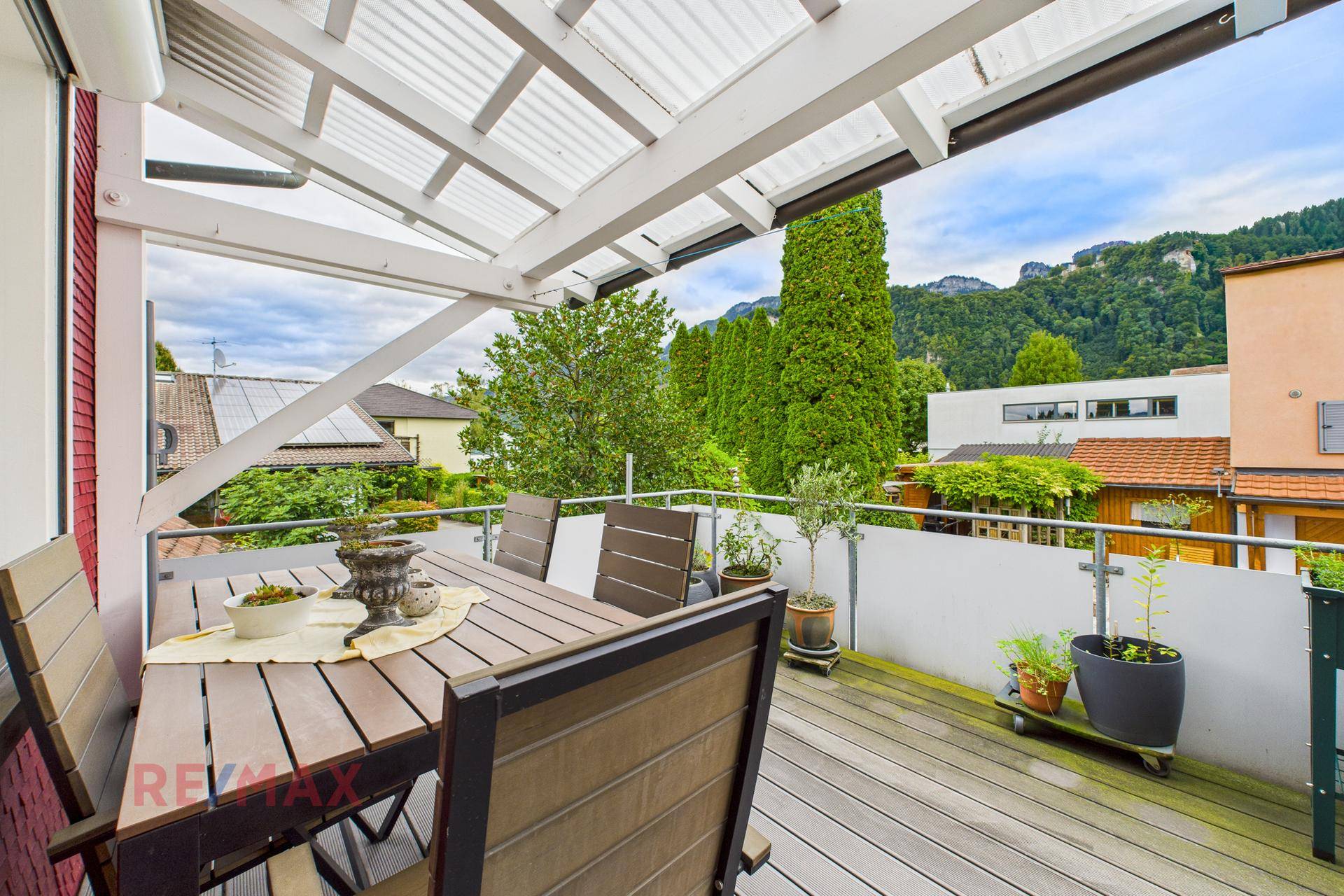 Geräumiger Balkon mit Holztisch, Stühlen und Blick auf die Berge und Bäume.