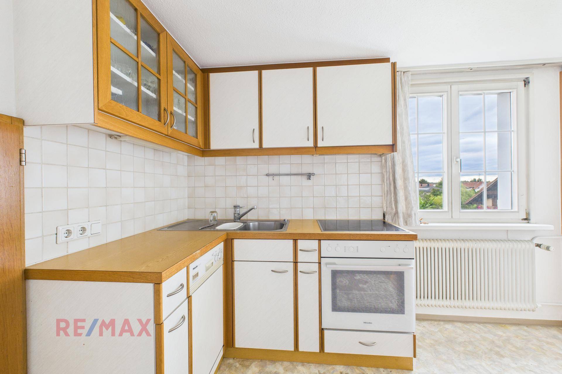 Einfache Küche mit weißen Schränken, Holztheke und Fensterblick.