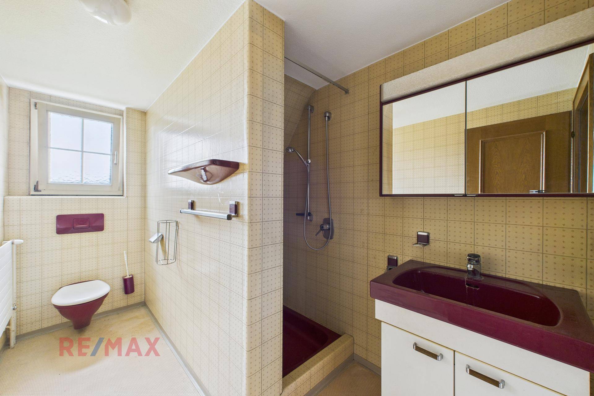 Badezimmer im Stil der 80er Jahre mit gelben Fliesen und rotem Waschbecken.