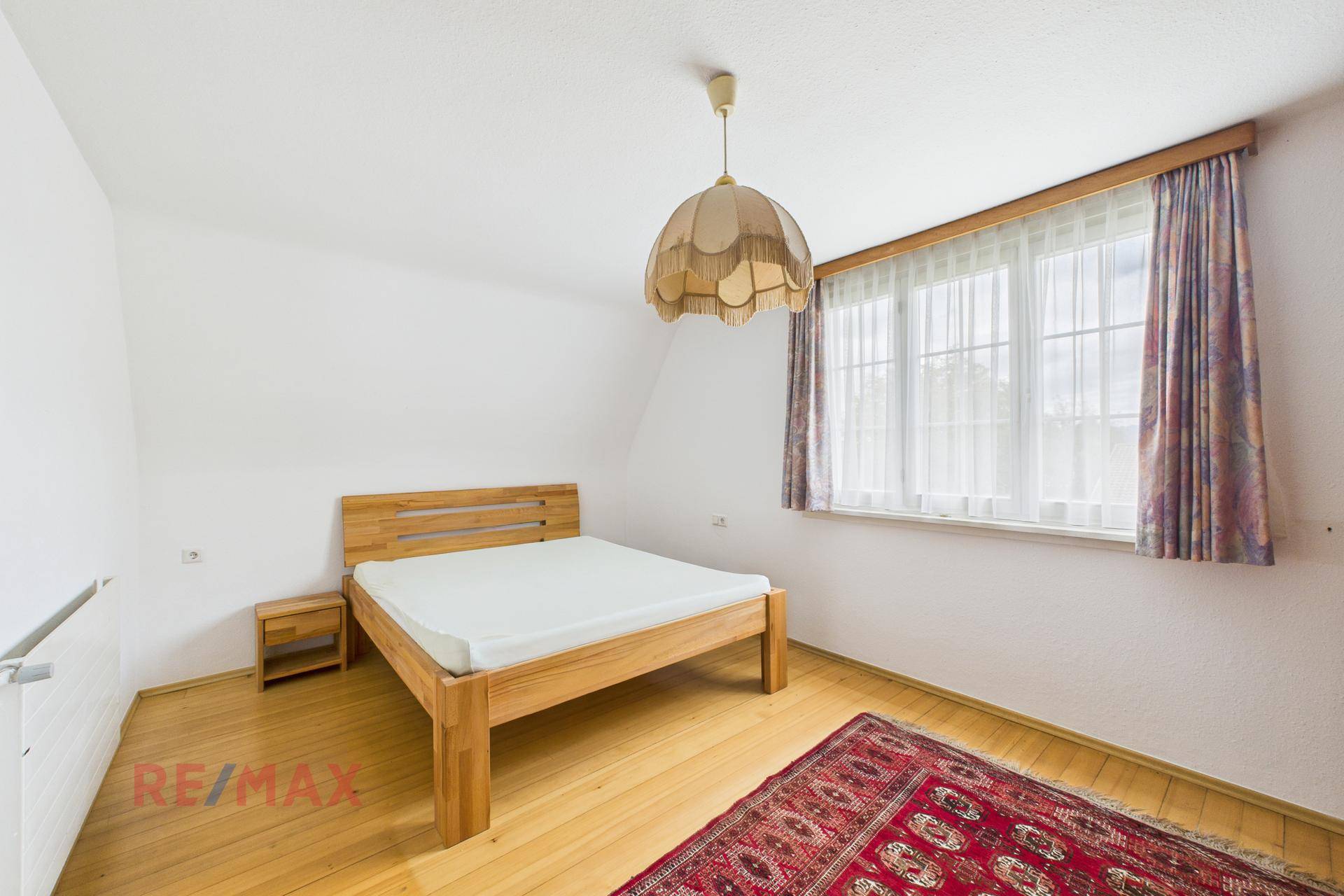 Helles Schlafzimmer mit Holzbett, Parkettboden und großem Fenster.