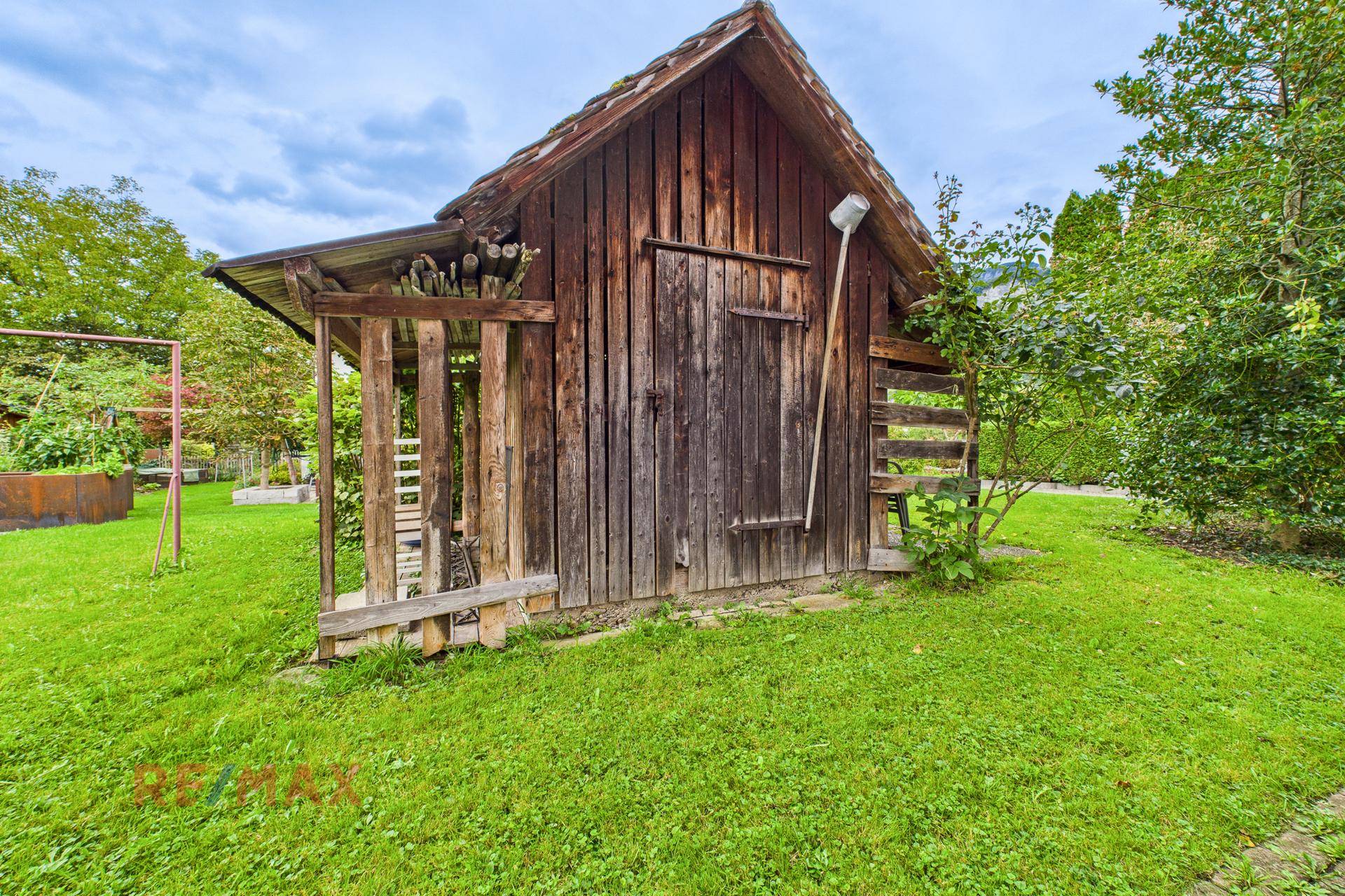 Rustikaler Holzschuppen im grünen Garten, umgeben von Rasen und Bäumen.