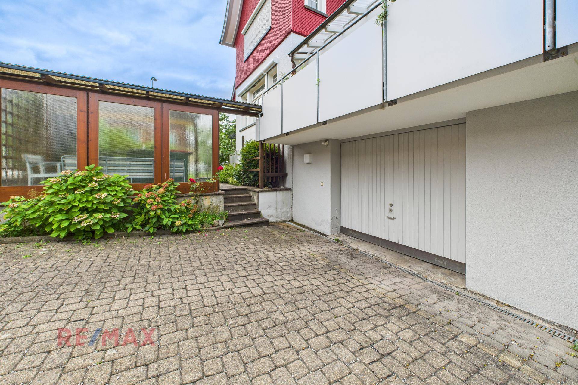 Einfahrt mit Pflastersteinen führt zu einer Garage, daneben eine überdachte Terrasse.