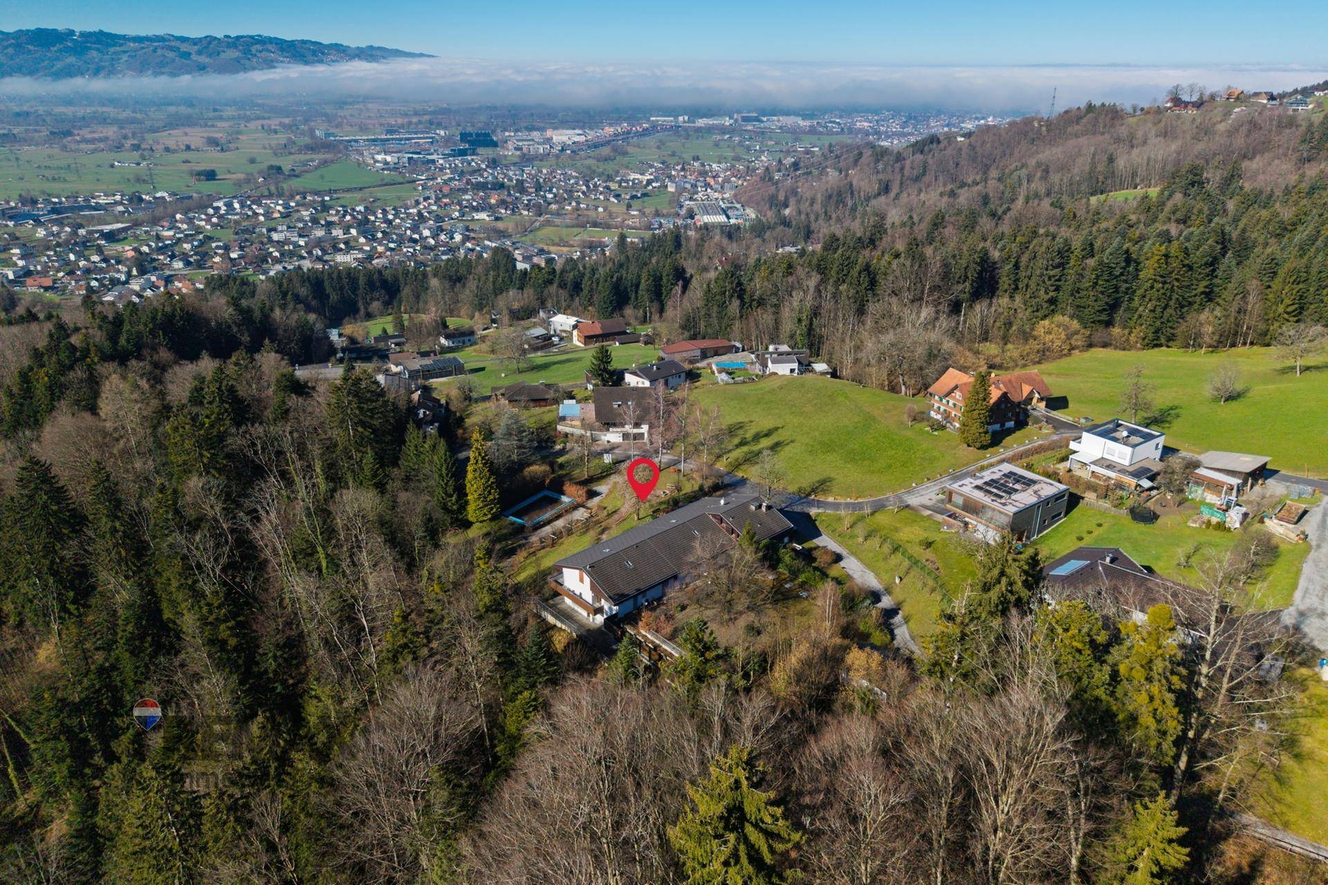 Weitläufige Luftaufnahme eines Anwesens in hügeliger Landschaft mit Blick auf eine Stadt in der Ferne.