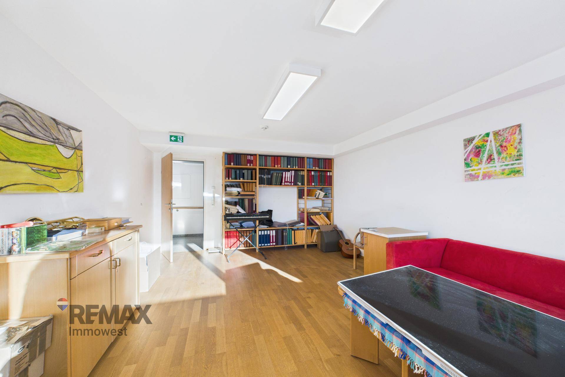 Geräumiger Gemeinschaftsraum mit Holzboden, Bücherregal und einem roten Sofa, ideal für Entspannung.