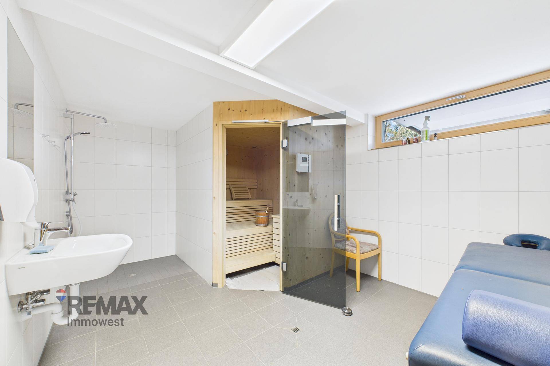 Wellnessbereich mit Sauna, Dusche und Liege, ausgestattet mit Fliesenboden und einem Fenster.