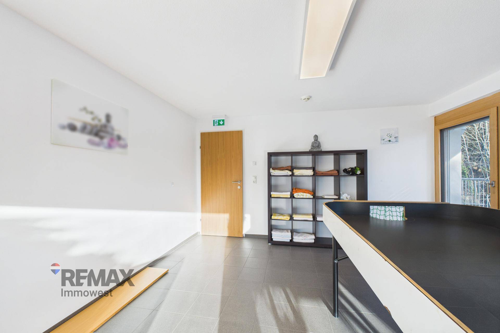 Freizeitraum mit Fliesenboden, Regal und Zugang zu einem Balkon, ideal für entspannte Stunden.
