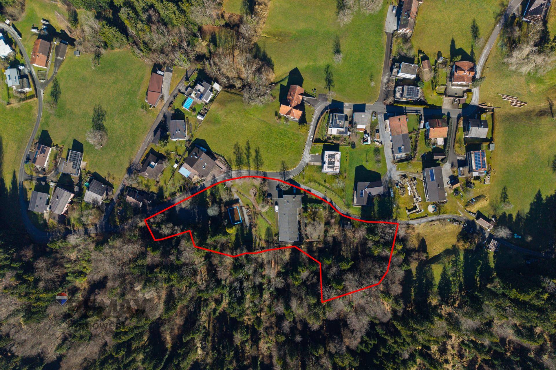 Übersichtliche Luftaufnahme des Anwesens mit markiertem Grundstücksbereich, umgeben von Wald und Häusern.