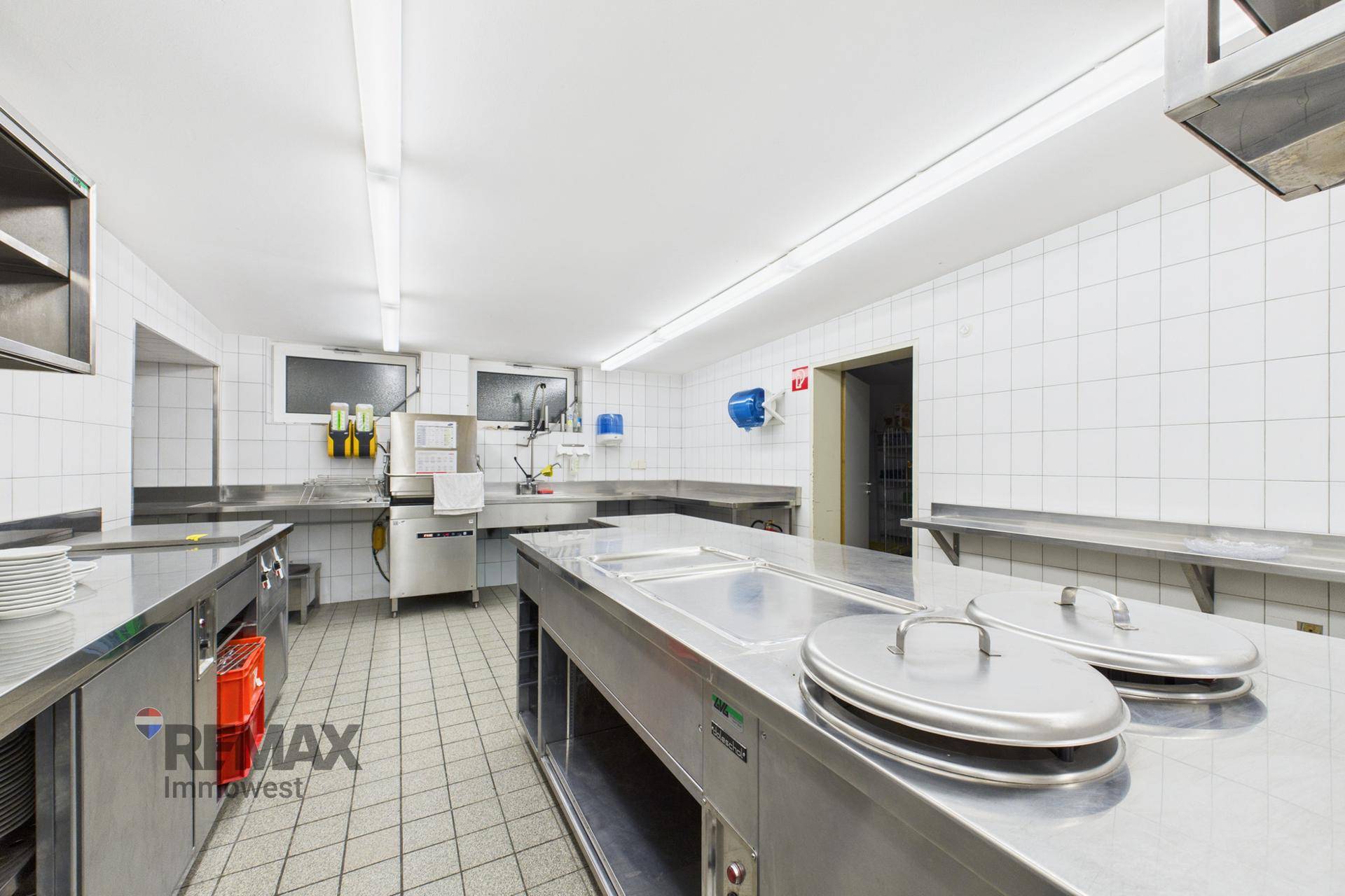 Professionelle Küche mit Edelstahl-Arbeitsflächen, Spülbereich und Fliesenwänden, bereit für den Betrieb.