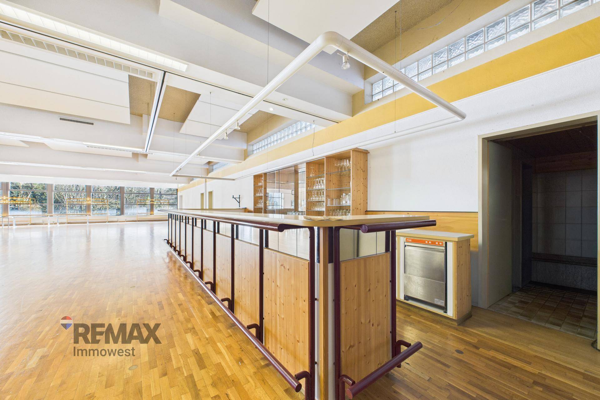 Geräumiger Saal mit Holzboden und einer langen Holzbar, bereit für Veranstaltungen und Bewirtung.