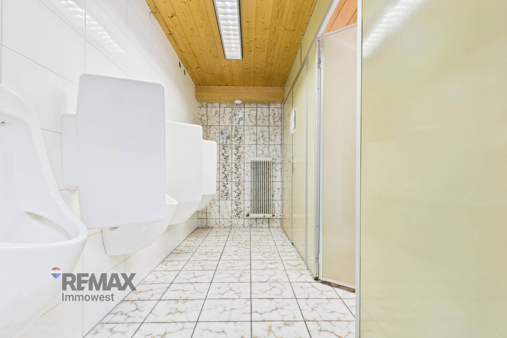 Öffentlicher Waschraum mit mehreren Urinalen, gefliesten Wänden und einer Decke aus Holzpaneelen.
