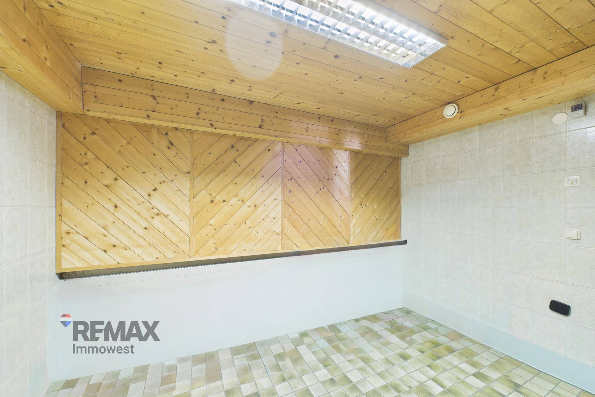 Raum mit Holzwänden und -decke sowie Fliesenboden, möglicherweise als Umkleide oder Lagerraum genutzt.
