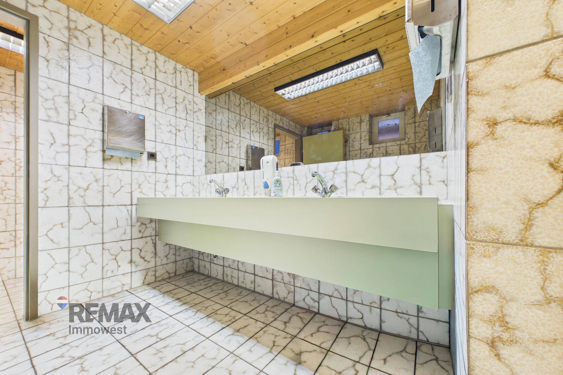 Geräumiger öffentlicher Waschraum mit mehreren Waschbecken, gefliesten Wänden und einer Holzdecke.