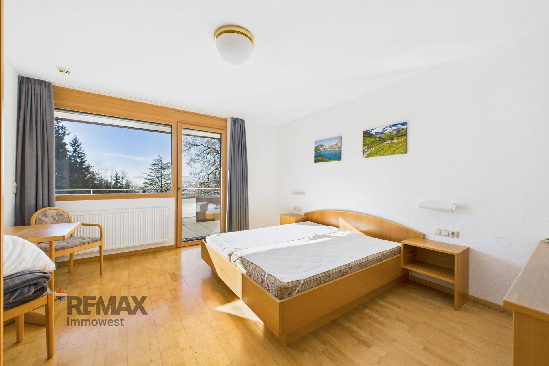 Helles Schlafzimmer mit Doppelbett, Holzmöbeln und großen Fenstern mit Zugang zum Balkon.