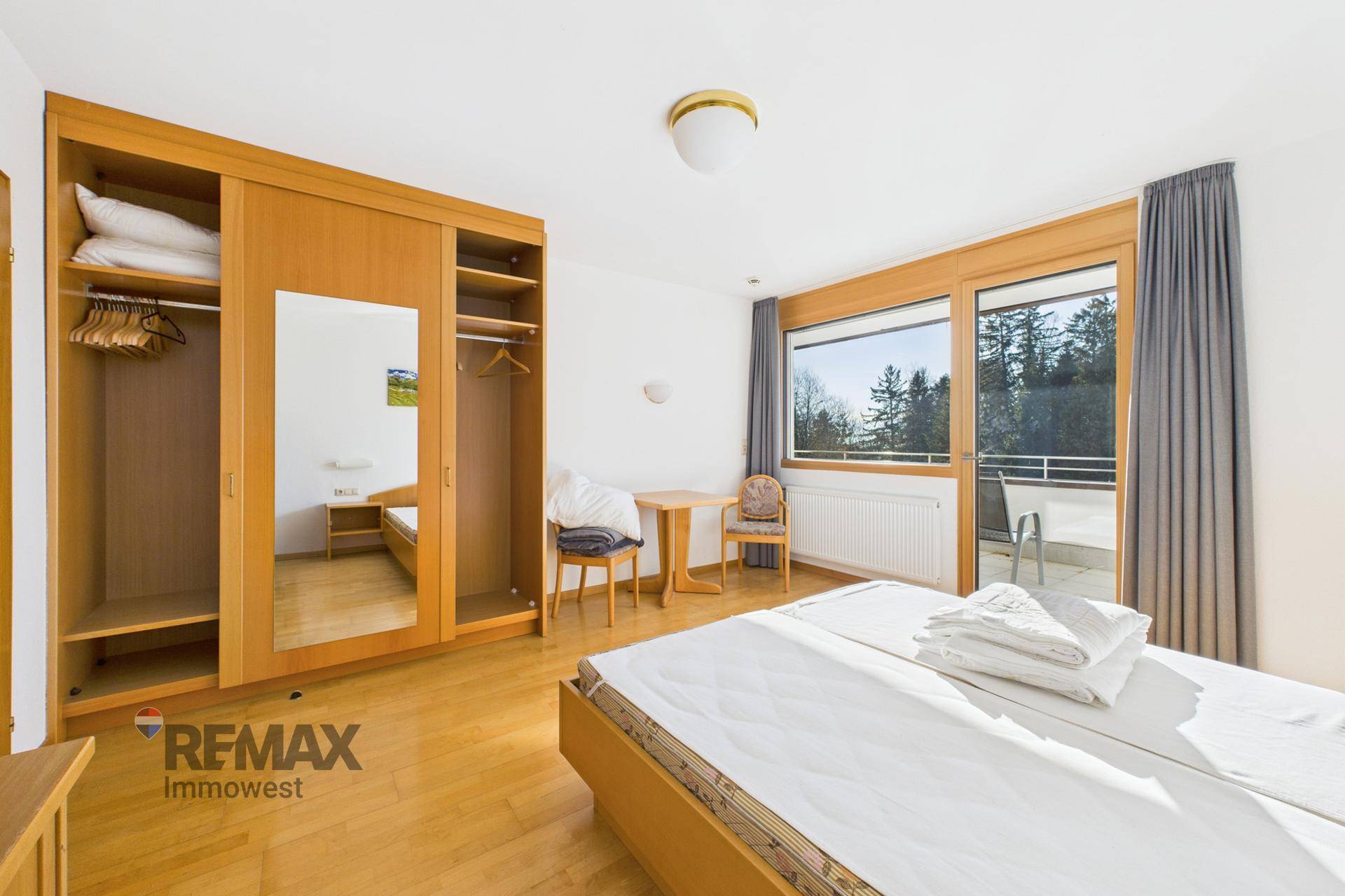 Gemütliches Schlafzimmer mit Doppelbett, großem Spiegelschrank und Zugang zu einem sonnigen Balkon.