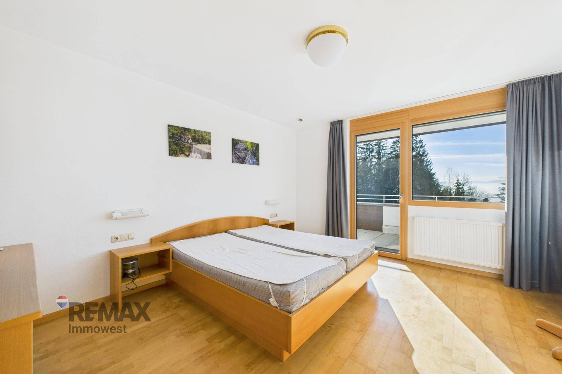Helles Schlafzimmer mit Doppelbett, Holzmöbeln und großen Fenstern mit Zugang zum Balkon.