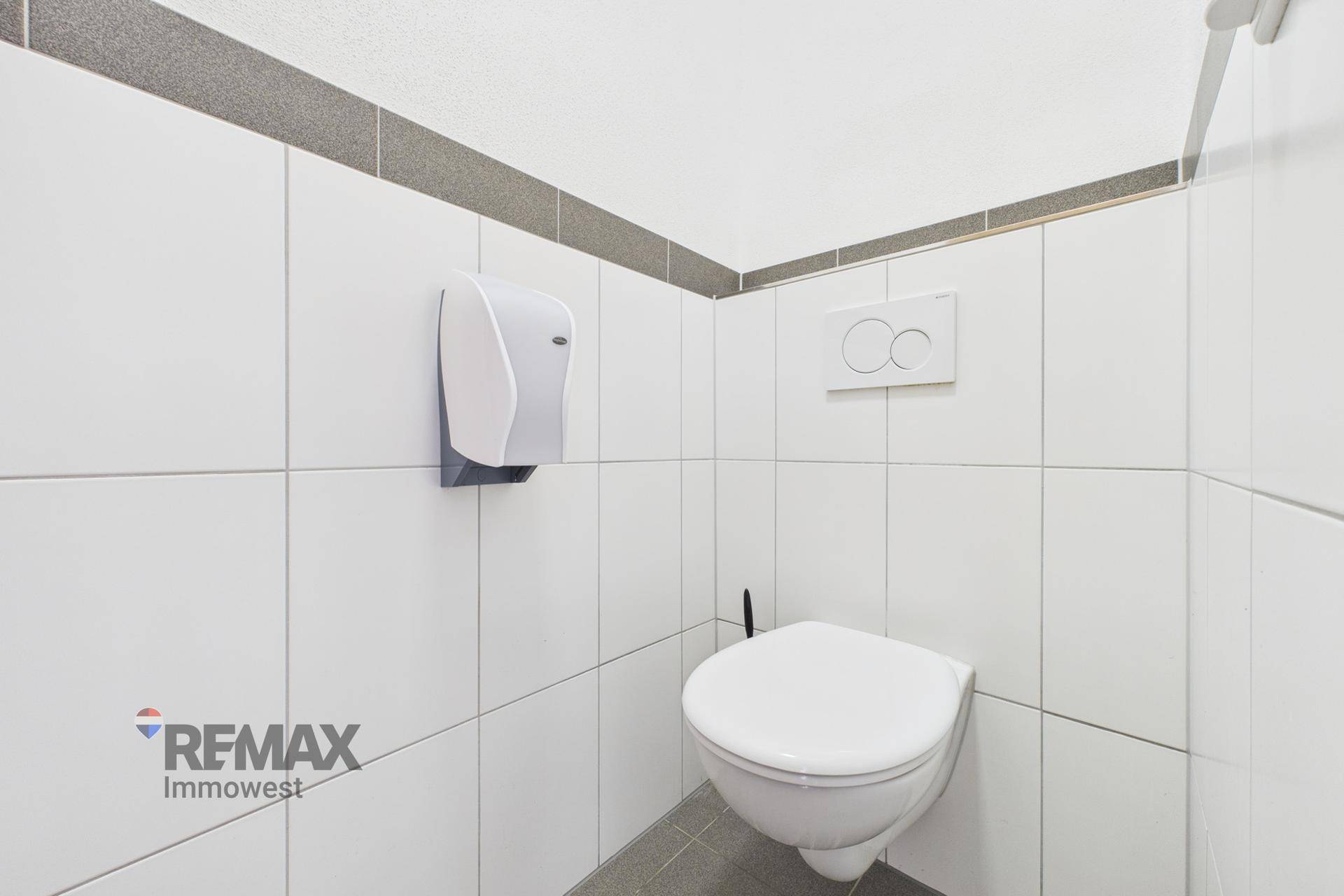 Saubere Toilette mit wandhängendem WC und weißen Fliesen, akzentuiert durch eine graue Bordüre.