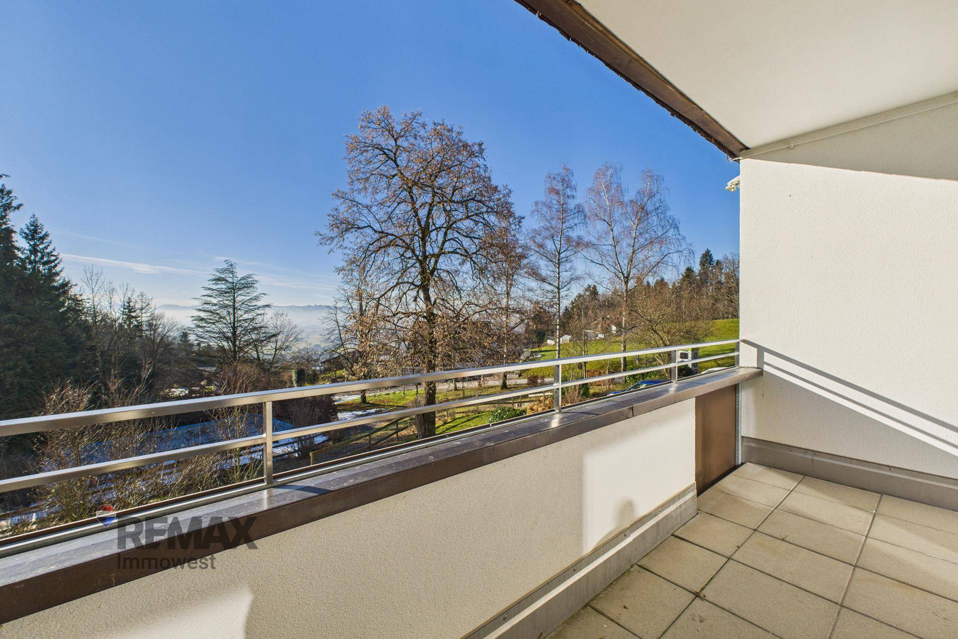 Geräumiger Balkon mit Fliesenboden und Metallgeländer, bietet einen weiten Blick ins Grüne.