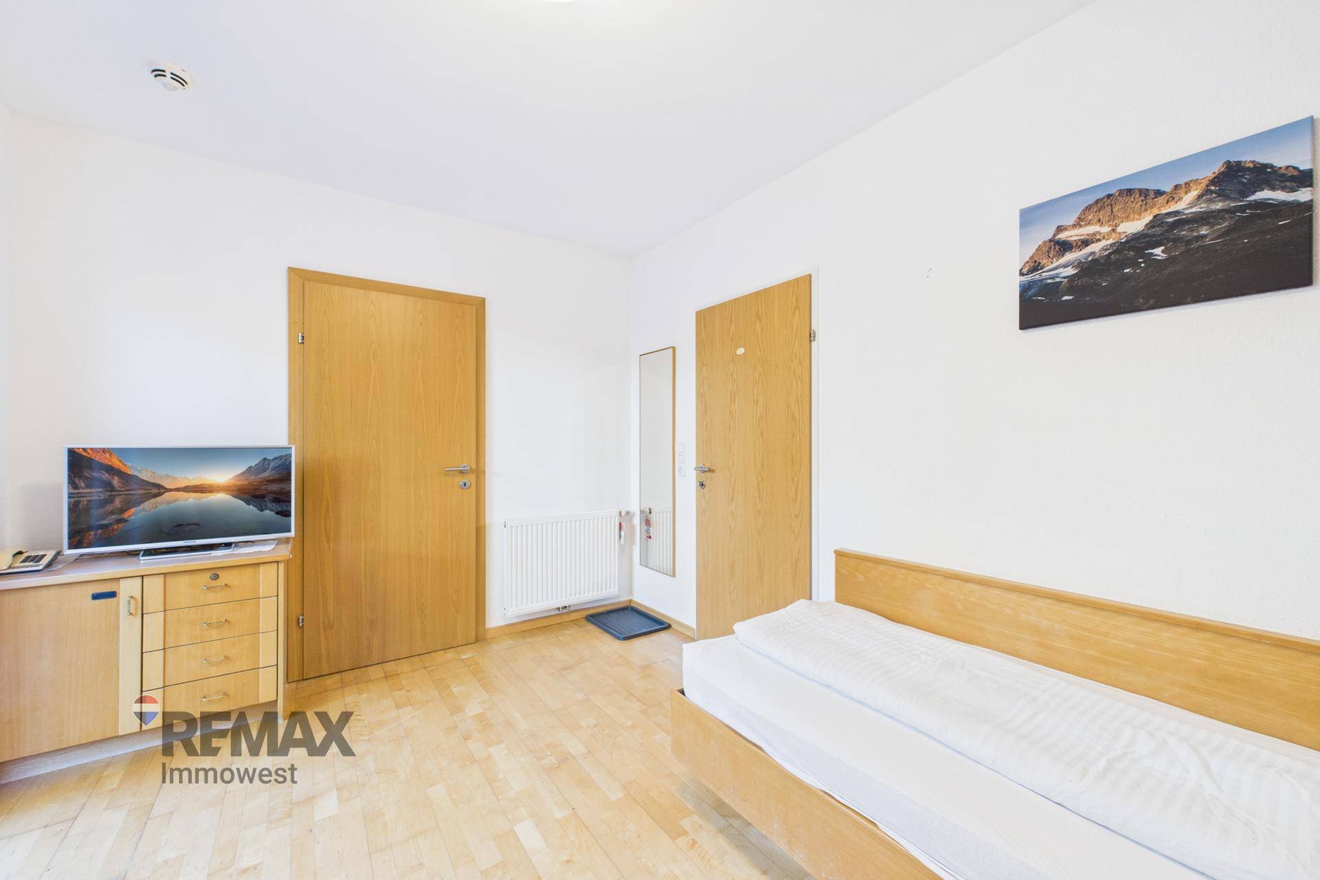 Gemütliches Schlafzimmer mit Holzboden, Fernseher auf Kommode und zwei Holztüren.