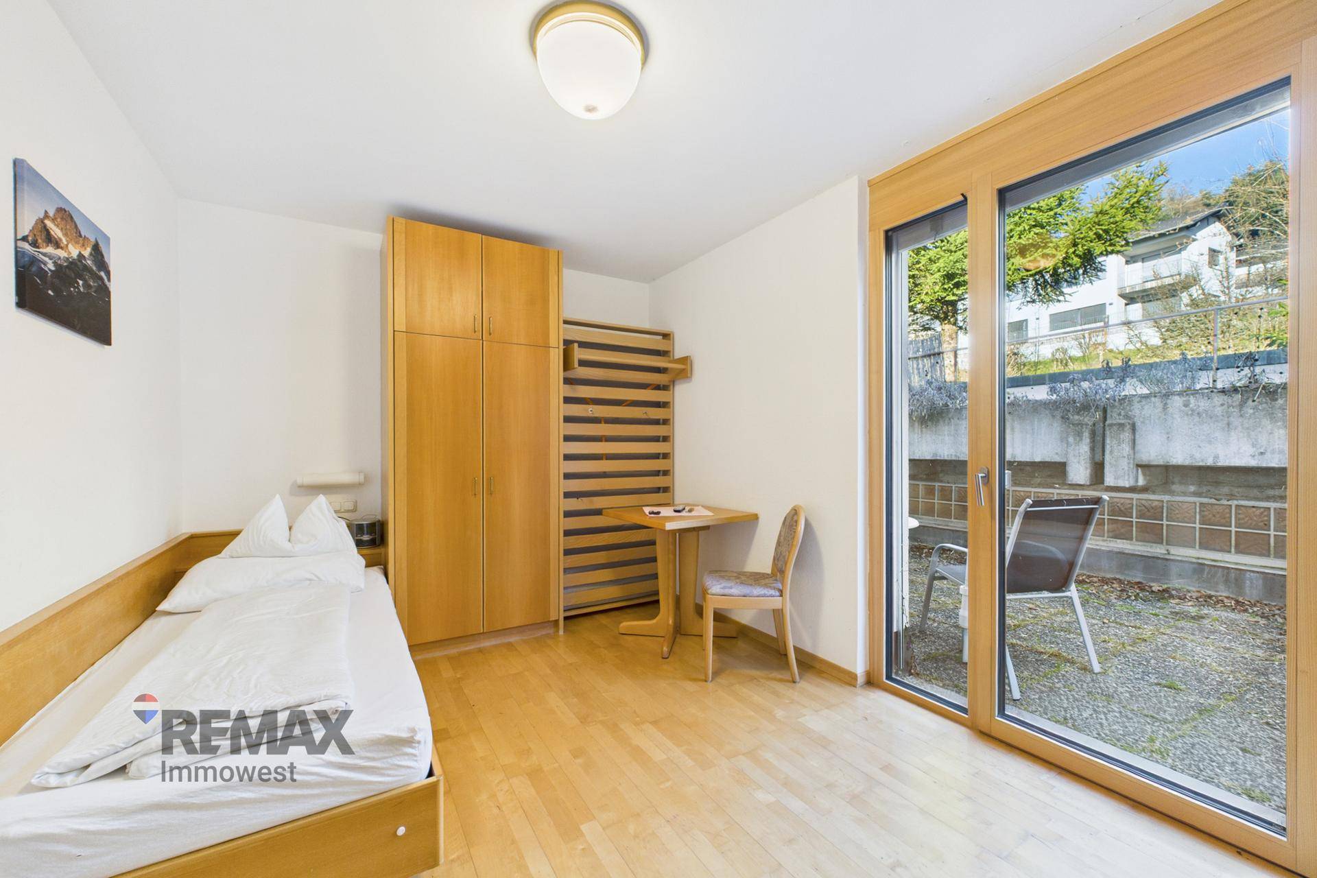 Helles Schlafzimmer mit Einzelbett, Holzschrank und direktem Zugang zu einer kleinen Terrasse.