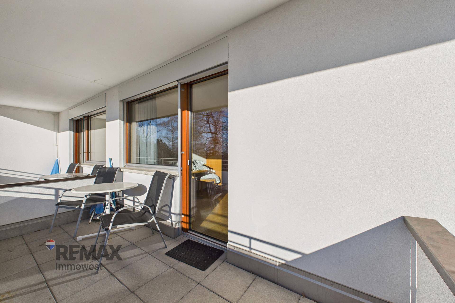 Heller Balkon mit Fliesenboden und Sitzgelegenheiten, direkt zugänglich durch eine große Glasschiebetür.