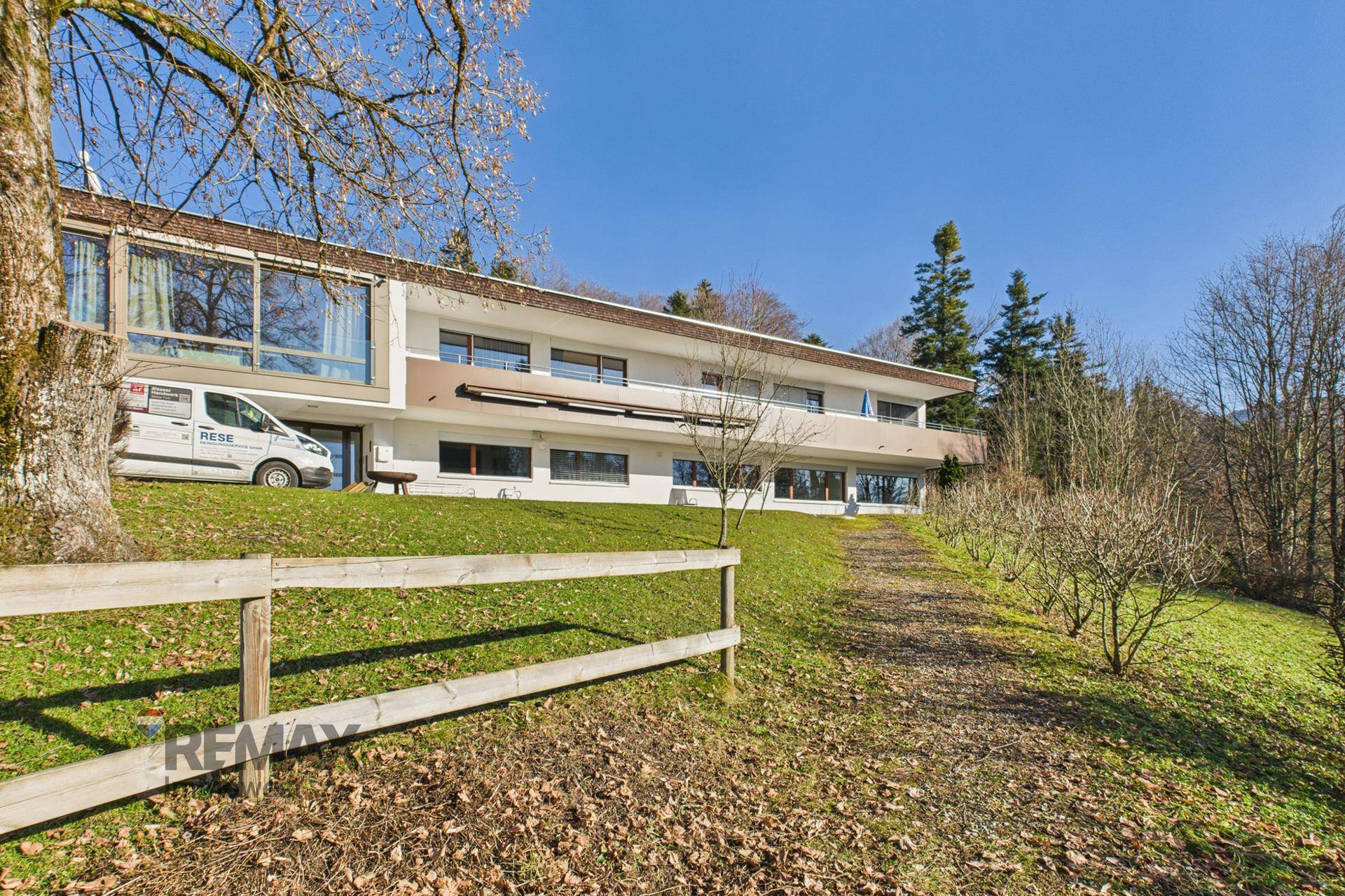 Moderne Gebäudefassade mit großen Fensterfronten und Balkonen, umgeben von viel Grün.