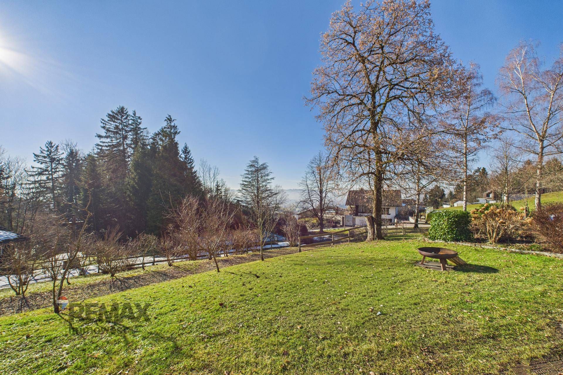 Weitläufiger Gartenbereich mit Rasenfläche, Bäumen und einem Feuerkorb, bietet eine weite Aussicht.