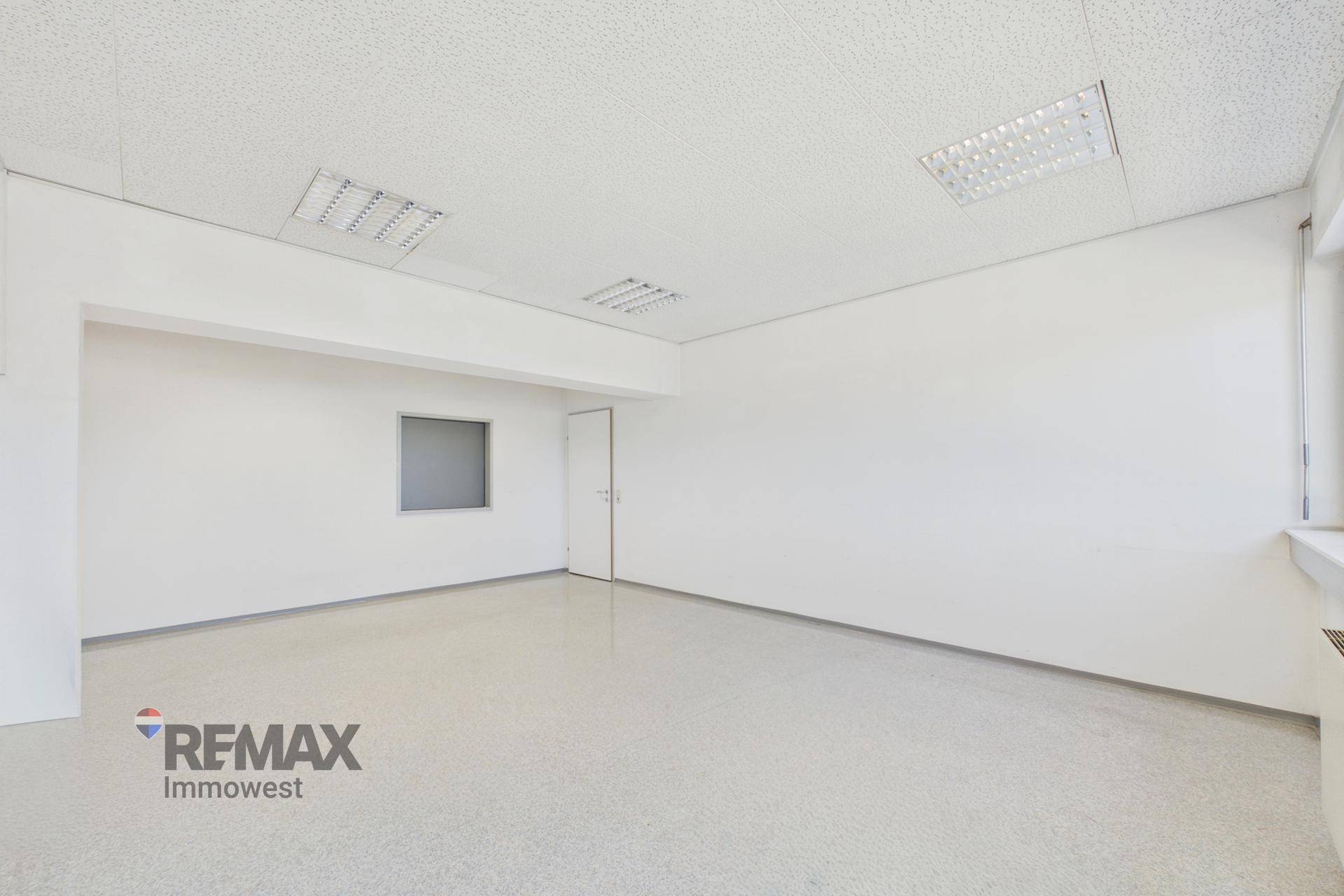 Leeres Büro mit glänzendem grauem Boden, weißer Tür und einer kleinen internen Fensteröffnung.